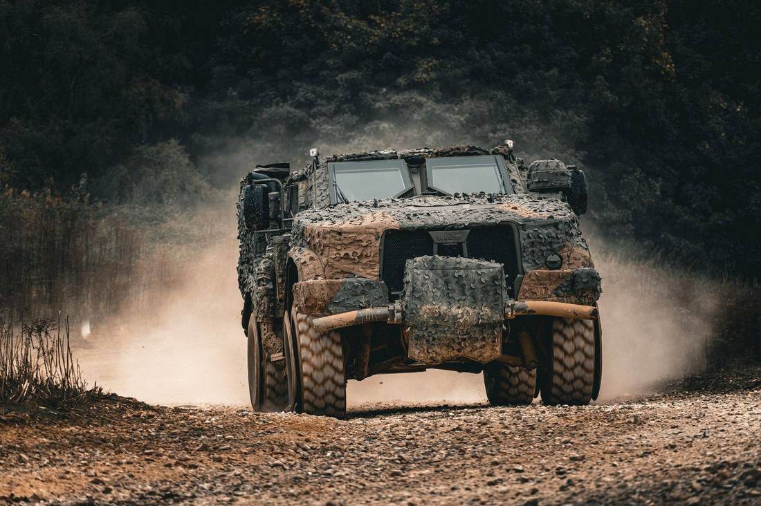 Camouflaged protected mobility vehicle kicking up dust on a gravel track